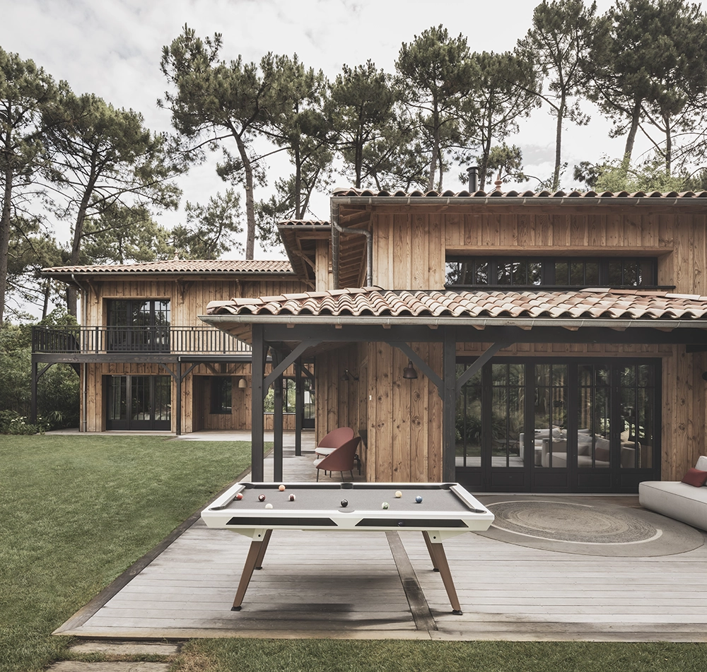 Table de billard d'extérieur blanche Cornilleau sur une terrasse contemporaine devant maison en bois