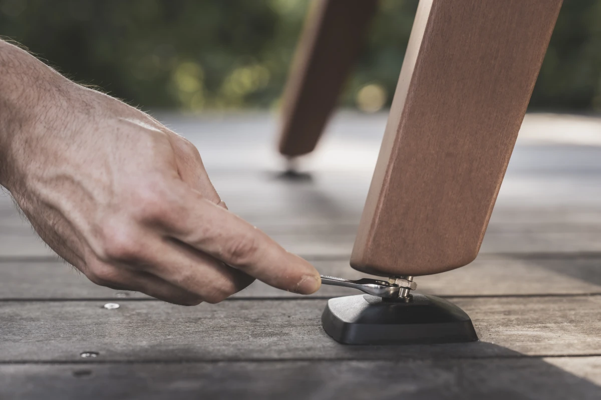Main ajustant le pied d’une table de billard Cornilleau sur une terrasse en bois.