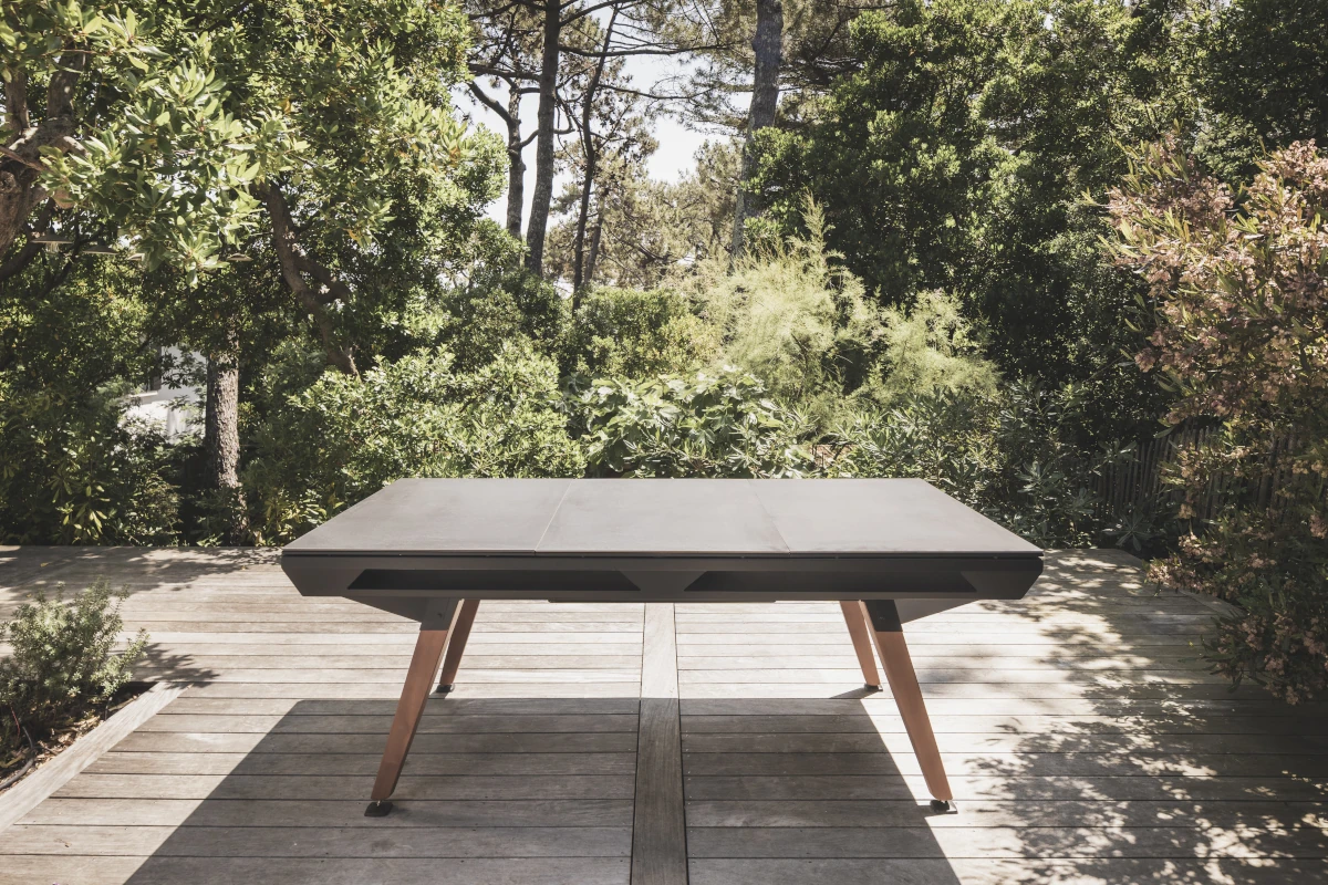 Table de billard Cornilleau installée en extérieur sur une terrasse entourée de végétation.