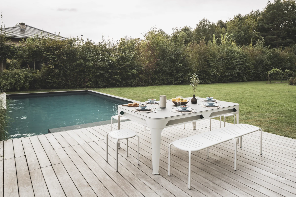 Billard convertible Cornilleau blanc utilisé comme table à manger sur une terrasse avec piscine et jardin.