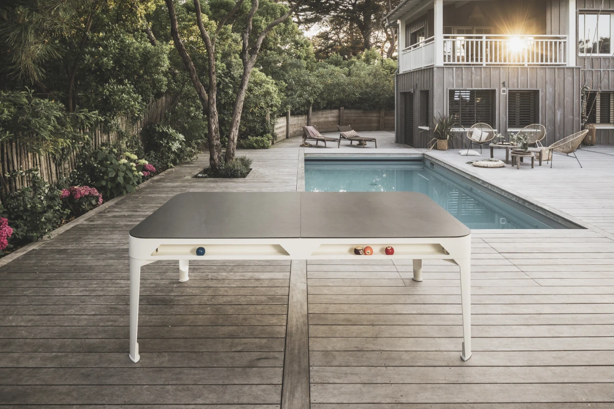 Billard convertible Cornilleau blanc fermé par ses plateaux sur une terrasse au bord d’une piscine.