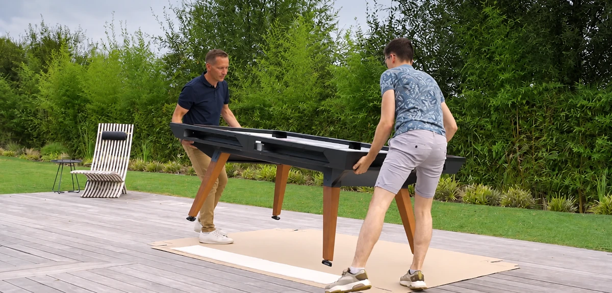 Deux personnes installent un billard d’extérieur sur une terrasse en bois.