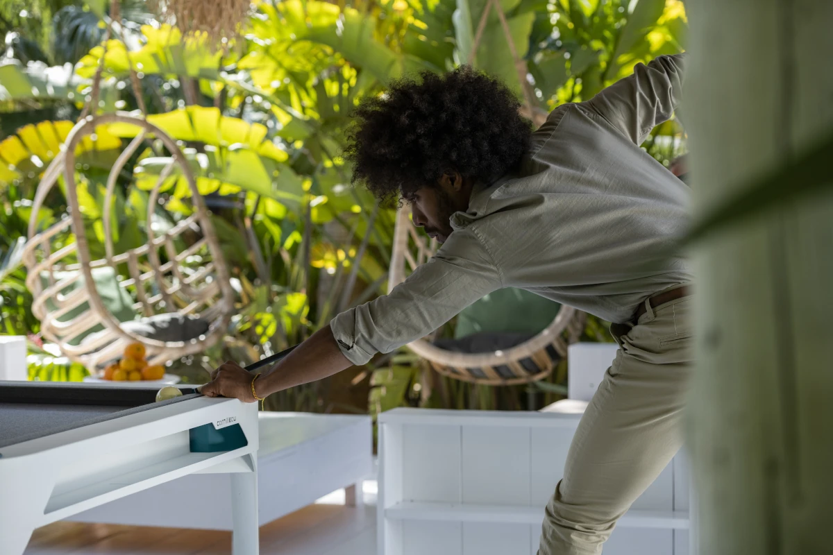 Joueur réalisant un coup sur un billard d’extérieur Cornilleau blanc installé sur une terrasse
