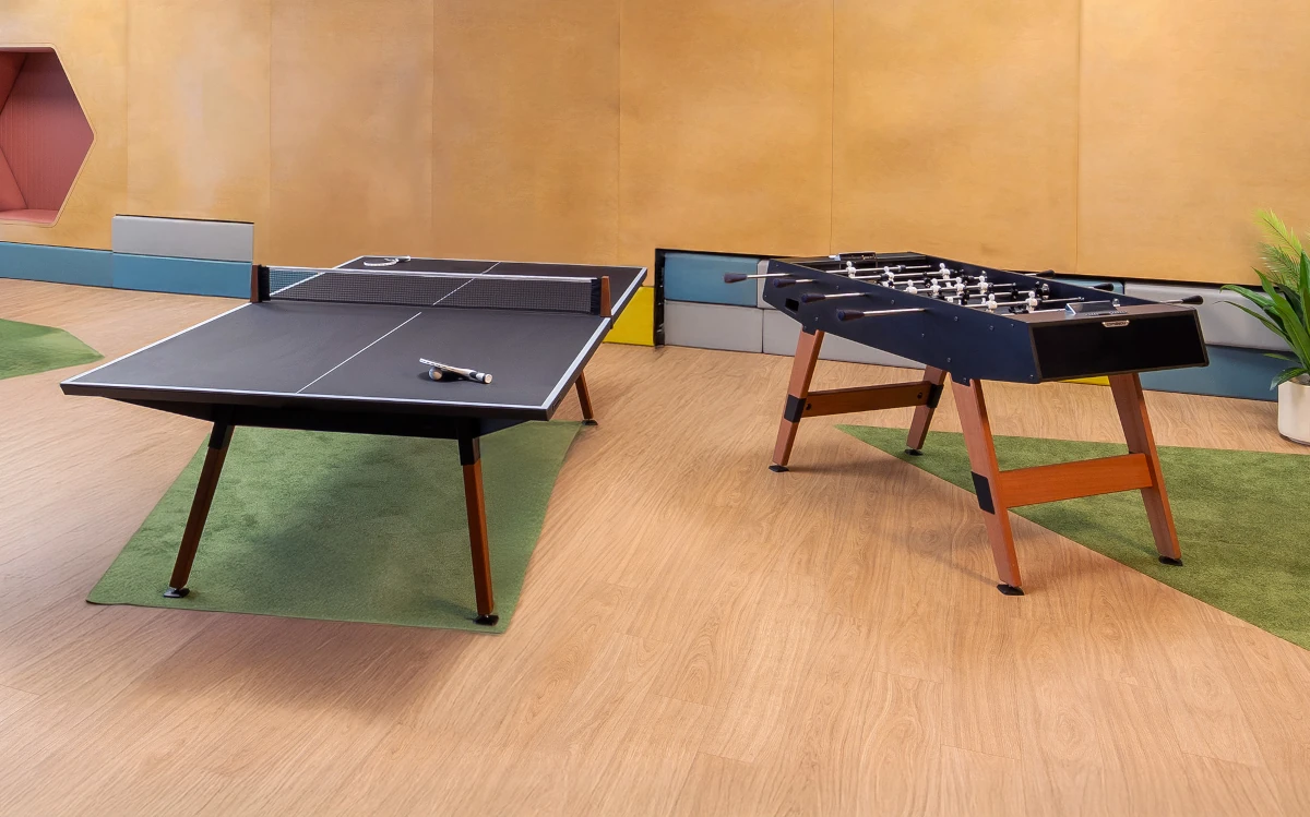 Table de ping-pong et baby-foot Cornilleau avec pieds en bois dans un espace de loisirs intérieur.